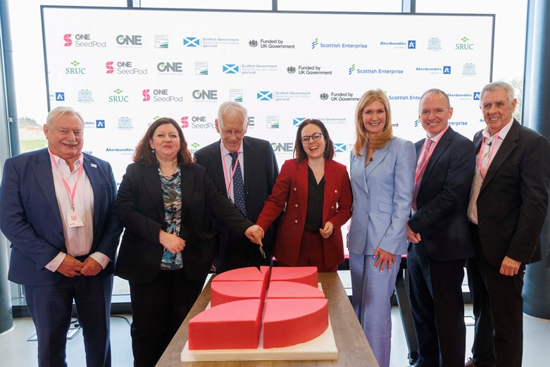 A group of people posing for a photo, while a cake is cut.