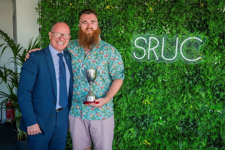 Two people smiling, one holding a trophy