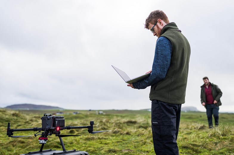 Man in a field with a laptop, using it to fly a drone.